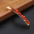 Macro shot of gold metal hair clip featuring natural red crystal stones on a wooden tray - Red Stone Gold