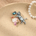 Close-up of a vintage rhinestone cat and house brooch displayed with elegant pearls - Grey Cat on Roof