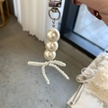 Detail of beaded pearl bow charm featuring three large white pearls and a silver clasp - White Beads