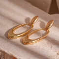 Detail of hollow oval drop earrings in gold finish against a natural stone background - Gold Oval Stud Earrings / Gold