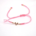 Macro shot of pink braided rope bracelet with a gold heart charm and pink zircon stones - Pink