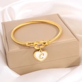 Gold twisted cable cuff bracelet with heart charm featuring letter C on beige jewelry box - Letter C