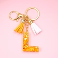 Close-up of resin letter L keychain with yellow stones and gold fringe tassels - L