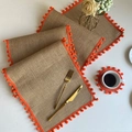 Vue détaillée du set de table en lin avec franges à pompons orange et texture tissée - Chemin de table en jute avec pompons rouge-orange