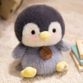Pinguin-Plüschtier aus weichem grau-weißem Plüsch mit rosa Wangen und Lederanhänger - Sitzender Pinguin