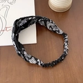 Elastic black paisley headband with a cross knot design shown on a wooden background - Black