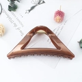 Elegant large brown triangle hair claw clip in a glossy resin finish on an open book - Jelly Copper
