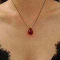 Detail of a red teardrop resin pendant on a slim black cord necklace worn by a model - Black Cord Red Gemstone Teardrop Necklace Style (WG-850)