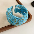 Detail van een meerlaagse hemelblauwe glaskraal armband met goud op houten ondergrond - Blauw