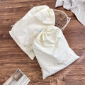 Detail of cream cotton drawstring bags featuring elegant tan embroidery on dark wood - Small (30x37cm) / Beige