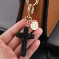 Cross keychain with black rhinestones and golden ring held against a brown bag - Black