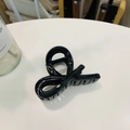 Detail of glossy black twist hair claw clip with cross design on a minimalist white table - Glossy Black