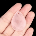 Pink quartz teardrop pendant with natural texture and pre-drilled hole held in hand - Rose Quartz