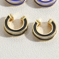 Macro view of C-shaped gold-tone ear cuffs with black and purple enamel drip finish - Black