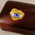 Macro detail of surrealist blue eye ring with gold-plated irregular metal frame on leather - Gold