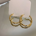 Dettaglio di orecchini a cerchio dorati con trama geometrica e design sfaccettato - Oro