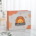 Süße orangefarbene Geschenktüte aus Papier mit Löwenmotiv und weißen gewebten Tragegriffen - Schüchterner Kleiner Löwe