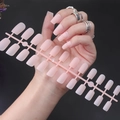 Hand holding matte nude long square press-on nails on a pink frame with dark background - Matte Nude