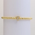 Macro detail of a gold beaded stretch bracelet with a pavé-set letter T charm - Letter T