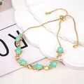 Nahaufnahme eines verstellbaren Hamsa-Armbands in Gold mit Emaille und bösem Blick-Charm - Grün