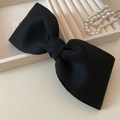 Detalle de un gran lazo de tela negra mate junto a perlas en un joyero elegante - Negro