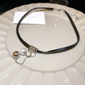 Detail eines schwarzen Lederchokers mit silbernen Metallakzenten und Perlenanhänger - Halskette-Schwarz-Weiß-Silber