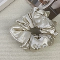 Close-up of a premium oversized champagne satin silk scrunchie with soft fabric pleats - Off-white