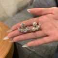 Orecchini asimmetrici in argento con strass e perle bianche mostrati sulla mano - Stile Curvo Asimmetrico / Argento