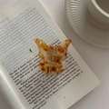 Detailed close-up of a butterfly hair claw with amber tortoise pattern on vintage book - Amber Yellow