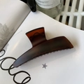 Macro detail of a large amber resin hair claw clip resting on minimalist white books - Matte Red Brown