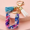 Macro view of resin letter U keychain with colorful gravel flakes and double suede tassels - Letter U
