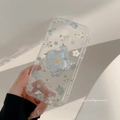 Close-up of clear phone case with blue floral patterns and matching flower grip stand - Blue White Flowers + Blue Flower Bracket / iPhone 15 Pro Max