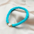 Bracciale di argilla blu lago con perla barocca naturale su sfondo di raso champagne - Celeste