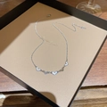 Detail van zilveren hartjes hangers met wit email op een beige kaart in een geschenkdoos - Zilver