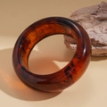 Macro detail of dark tortoiseshell resin bangle resting on natural stone with warm tones - Amber Tortoiseshell Smooth Wide