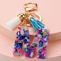 Detail of letter M resin keychain with colorful stones and blue white tassels - M