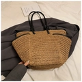 Detail of a large straw tote bag featuring contrast black handles on a soft fabric backdrop - Khaki