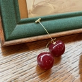Detail view of red cherry earrings with gold stems placed on a rustic wooden table - Large Dark Red Solid Color