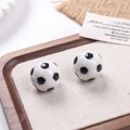 Gros plan de boucles d'oreilles miniatures football noir et blanc sur un plateau bois - Petit football
