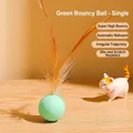 Green elastic cat toy ball with natural brown feathers on a wooden desktop surface - Green