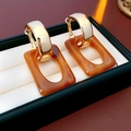 Detalle de pendientes C dorados con colgante de resina ámbar en caja de joyas negra - Estilo de Colgante de Ámbar / Marrón dorado