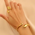 Primo piano di un set di gioielli dorati a goccia con anello e bracciale rigido aperto - Set Bracciale e Anello con Linea Organica a Goccia