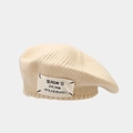 Detail of cream knitted beret featuring a branded fabric label and thick wool texture - Beige