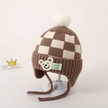 Detail van baby gebreide muts met bruin schaakbordpatroon, beerpatch en witte imitatiebont pompon - Lichtkoffie