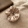 Gros plan du chouchou en satin champagne avec plis doux sur fond en tricot douillet - Blanc Cassé