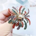 Détail d'une luxueuse broche fleurie avec strass colorés et une perle centrale - Multicolore