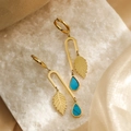 Pendientes de hoja dorada con gota azul sobre superficie de piedra y fondo de seda - Azul