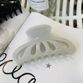 Dettaglio di una pinza per capelli color bianco crema a forma di petalo su sfondo libro - Grigio Gelatina