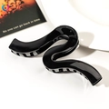 Close-up of a glossy black S-shaped hair claw clip with elegant minimalist curves - 13cm Geometric Wave - Shiny Black