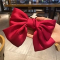 Handheld view of a large red velvet hair clip with a full-bodied satin bow structure - Premium Satin - Red